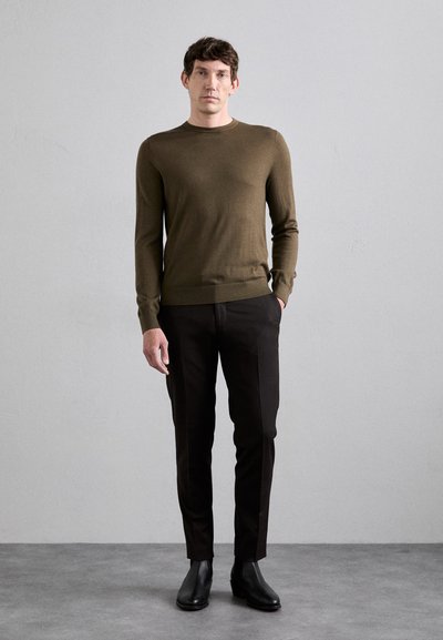 Olijfgroen gebreid sweater met een ronde halslijn, gecombineerd met aansluitende zwarte broeken en zwarte enkellaarsjes. Zachte textuur, eenvoudig ontwerp.