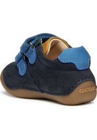 Scarpa in suede navy con dettagli blu, cinturini con chiusura a strappo, punta rotonda e suola in gomma beige. Presenta cuciture a vista e il marchio Geox.