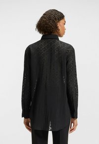 Camicia nera con bottoni, in tessuto texture, maniche lunghe e colletto, con un motivo discreto sul retro.