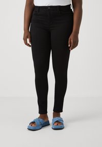 Svarta, kroppsnära byxor gjorda av ett mjukt, elastiskt material. Kombineras med blå, texturerade sklipp-on sandaler med ett kors och tvärs-mönster.
