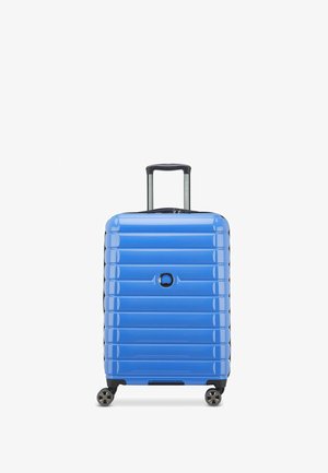 Maleta rígida de color azul brillante, diseño acanalado, asa retráctil, cuatro ruedas, detalles en negro, logotipo circular en el centro. Textura suave.