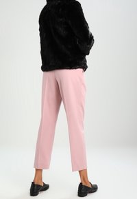 Giacca in ecopelliccia nera, pantaloni rosa chiaro con taglio affusolato e ballerine nere. Focus sulle texture e sul contrasto di colori.