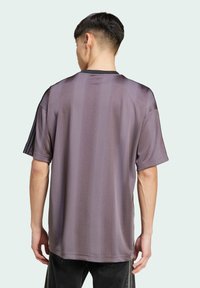 Fialová pruhovaná košile s krátkým rukávem, kulatým výstřihem a hladkou texturou. Vyznačuje se kontrastními černými detaily na ramenou.