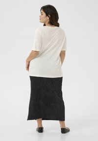 Beige top met korte mouwen en een ontspannen pasvorm, gecombineerd met een lange zwarte rok met een gestructureerd patroon en een zijsplit, gedragen met zwarte schoenen.