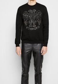 Svart sweatshirt med rund halsringning, som har ett dekorativt mönster av silvernitar i en invecklad design, samt texten "RICHMOND" nederst.