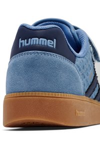 Niebieski zamszowy tenisówka o teksturowanym wzorze, z paskiem na rzep, ciemnoniebieskimi akcentami i gumową podeszwą w kolorze naturalnej gumy. Logo umieszczone na tylnej części.