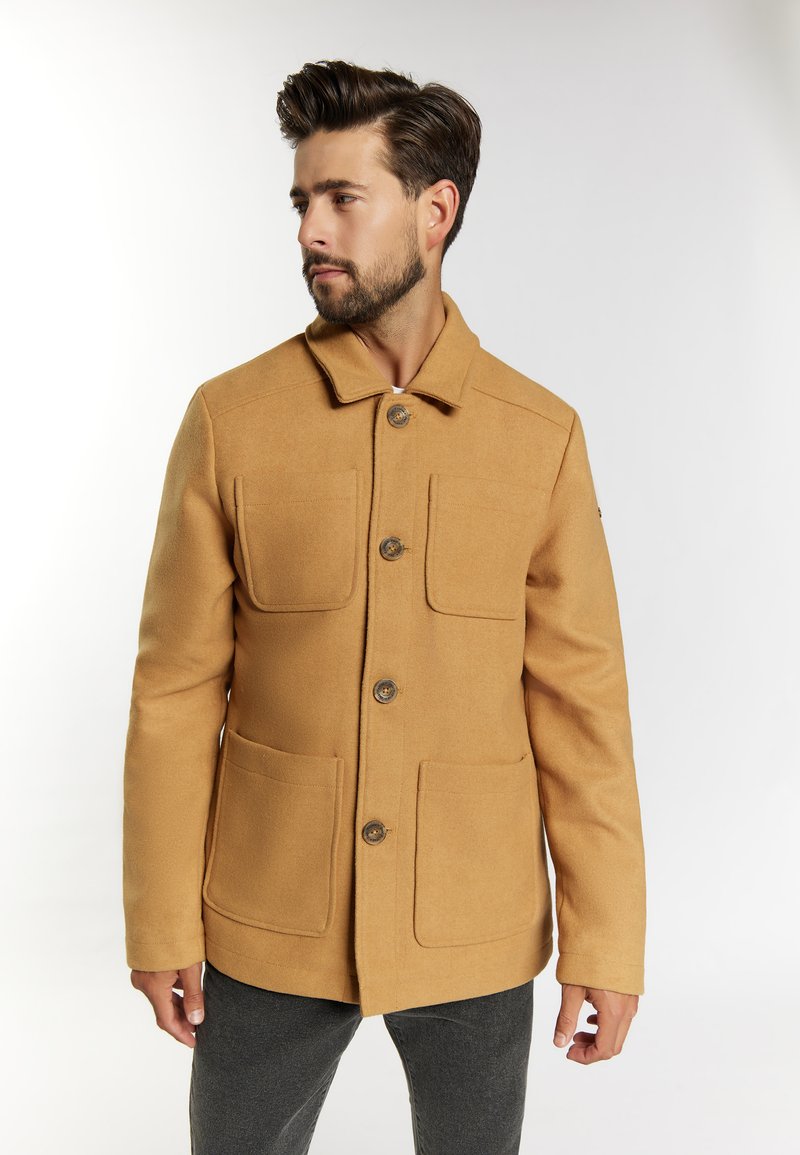 Manteau en mélange de laine couleur sable avec un col, doté de quatre poches avant et d'une fermeture à boutons. Texture lisse et coupe ajustée, conçu pour être porté en superposition.
