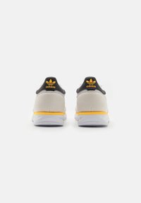 Adidas-sneakers i grått och svart, med en gul accent på sulan. Mjukt mockamaterial med vadderad krage och logotypdetalj.