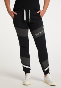 Schwarze Jogginghosen mit grauen Streifen, ausgestattet mit einem elastischen Bund, Kordelzug und Logodetail. Hergestellt aus weichem, strukturiertem Stoff.