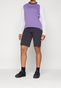 Långärmad lila och vit skjorta som matchas med svarta shorts; tyget känns andningsbart, med en avslappnad passform och minimala varumärkesdetaljer. Svarta sneakers.