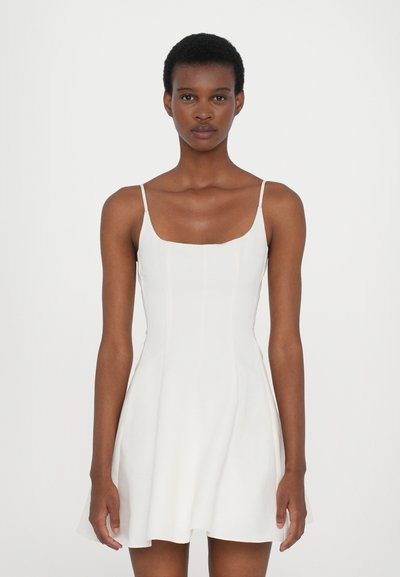 Vestido mini blanco con tirantes finos, corsé ajustado, falda acampanada, tejido texturizado y sutilezas en las costuras.