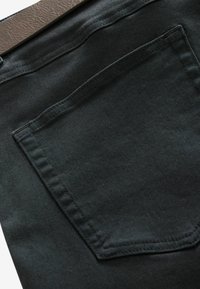 Tejido de mezclilla negra con un bolsillo trasero con bordes cosidos y una textura suave, expuesto sobre un fondo neutro.