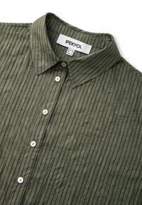 Chemise boutonnée en tissu vert olive froissé avec rayures verticales et col pointu, montrant l'étiquette de la marque et les tags de taille à l'intérieur.