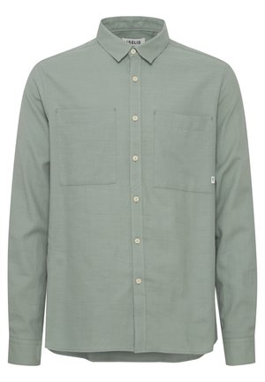 Jasnozielona koszula z długim rękawem wykonana z tkaniny o gładkiej fakturze. Posiada kołnierz w szpic, dwie kieszenie na piersi oraz zapięcie na guziki.
