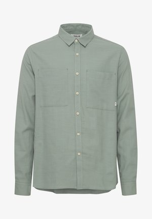 Lys grønn langermet skjorte laget av stoff med en glatt tekstur. Har en spiss krage, to brystlommer og knappestolpe.