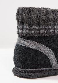 Zwarte vilten slippers met een gebreide grijze boord. Heeft een geweven grijs patroon en een gestructureerde zool. Zacht, warm materiaal met contrasterende accenten.