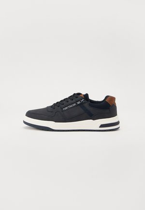 Námořnické sneakers s texturovaným síťovaným svrškem a hladkými koženými akcenty. Bílá mezipodešev, tmavá podrážka a jemné značení na boku.