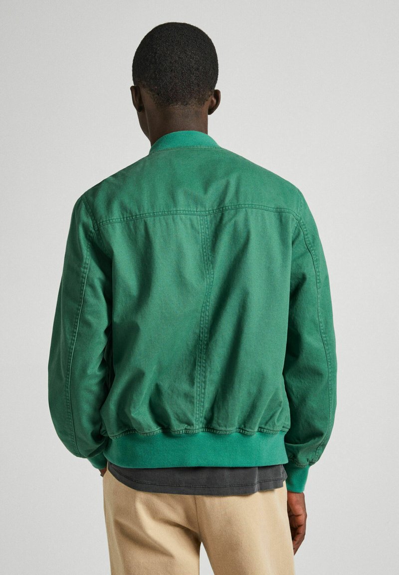 Chaqueta bomber verde con dobladillo y cuello acanalados, hecha de tela ligera. Presenta líneas limpias y un corte relajado.