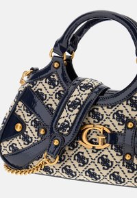 Marine patentlæderdetaljer på en cremefarvet taske med et mørkt blomsterdesign, en guldkrog og dekorative hardware detaljer.