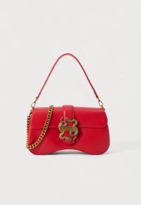 Borsa a mano in pelle rossa con forma curva, tracolla a catena dorata e emblema decorativo a forma di serpente sulla chiusura. Texture liscia e design strutturato.