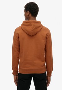 Bruine hoodie met een ontspannen pasvorm, voorzien van een capuchon met trekkoord, geribbelde manchetten en zoom. Gladde textuur, gecombineerd met zwarte broek.