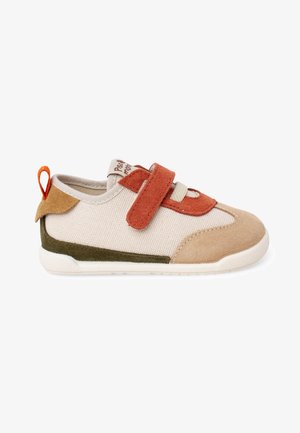 Zapatilla para niño pequeño beige y marrón con detalles en naranja y oliva, cierre de velcro y presilla en una suela blanca.