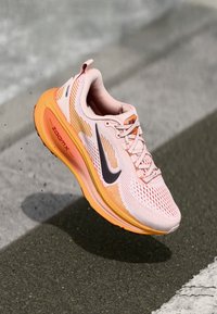 Zapatilla de correr de color rosa claro con acentos naranjas, parte superior de malla, cuello acolchado, logo Swoosh negro y amortiguación ZoomX en la suela.