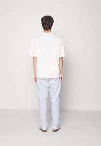 Bílá bavlněná tričko s krátkým rukávem, spárované se světle šedými tepláky. Oblečení má volný střih a jednoduchý design.