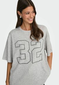 Szara, oversize koszulka z krótkim rękawem, z czarną, wysadzaną ćwiekami liczbą "32" na przodzie. Miękka tekstura, swobodny krój.