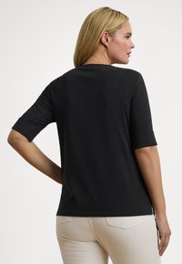 Μαύρο κοντομάνικο τοπ από απαλό ύφασμα, με χαλαρή εφαρμογή, στρογγυλή λαιμόκοψη και μανίκια με μανσέτες. Απλός και μινιμαλιστικός σχεδιασμός.