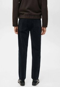 Pantalones de pana azul oscuro con dos bolsillos traseros, diseño de pierna recta y textura sutil. Combinados con un suéter marrón ajustado.