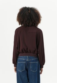 Burgunderfarget genser med ribbestrikket kant og myk tekstur; har avslappet passform og lange ermer kombinert med blå høytlivede jeans.