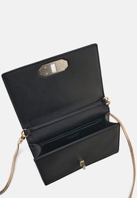Schwarze Leder-Crossbody-Tasche mit einem goldenen Kettenriemen, ausgestattet mit einer Innen-Tasche und einem dekorativen goldenen sowie texturierten Verschluss.