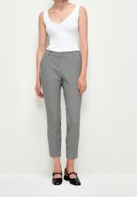 Pantalon à carreaux vichy noir et blanc, coupe slim, en tissu lisse, avec poches latérales et longueur chevilles. Porté avec un haut blanc.