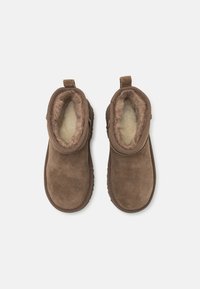 Botas de tobillo de ante marrón con suave forro de pelo sintético y tira para facilitar su puesta. Punta redondeada, suela plana y costuras decorativas a lo largo de los bordes.