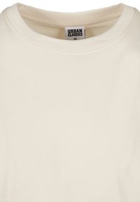 Gros plan d'un t-shirt beige à col rond avec une étiquette de la marque Urban Classics en taille medium visible à l'intérieur du col.