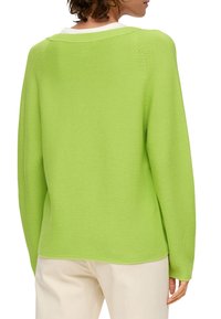 Grüner Strickpullover mit lockerer Passform, breitem Ausschnitt und strukturiertem Muster, kombiniert mit cremefarbenen Hosen.