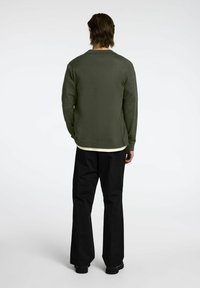 Chaki spalvos džemperis su tekstūru ir laisvu kirpimu, derinamas su juodomis plačiomis kelnėmis ir tvirtu juodu apavu.