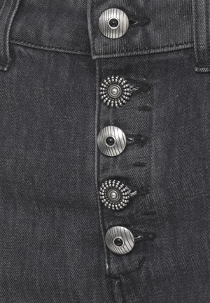 Primo piano di tessuto in denim scuro che mostra quattro bottoni metallici decorativi con disegni circolari alternati lisci e perlati.