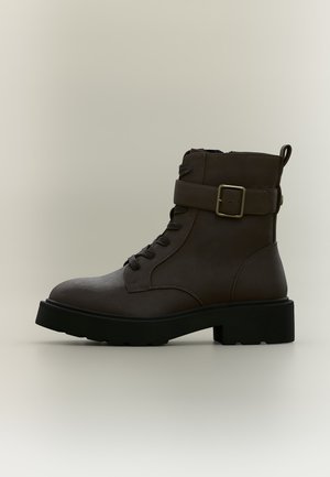 Dunkelbrauner Leder-Stiefelette mit schwarzer dicker Sohle, Schnürung vorne und verstellbarem Riemen mit Metallschnalle an der Seite.
