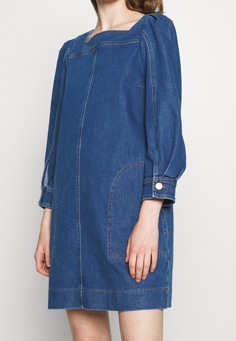 Abito in denim con scollatura quadrata e maniche a sbuffo. Presenta due tasche laterali e cuciture a contrasto. Lunghezza fino a metà coscia.