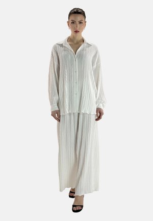 Conjunto blanco texturizado de dos piezas que incluye una camisa con cuello y botones, y una falda larga a juego, con una silueta fluida y patrones visibles.