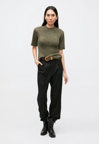 Olivovo zelený pletený sveter s krátkymi rukávmi, v kombinácii s vysokým pásom čiernych nohavíc a hnedým opaskom. Čierne členkové topánky dopĺňajú outfit.