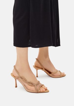 Sandali nudi con cinturini in materiale trasparente, caratterizzati da un design incrociato e dettagli metallici. Tacco a stiletto sottile e punta aperta.