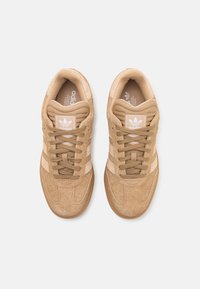 Beige semskede sneakers med snøring, hvite detaljer og tre striper. Har polstret tunge og dempet såle, flat gummisåle.