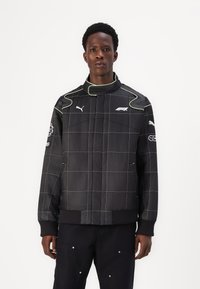 Black padded jacket with grid pattern, green accents, high collar, and logo on chest and sleeve. Features ribbed cuffs and hem.