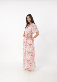 Robe maxi florale avec une base rose clair ornée de fleurs rouges et turquoise, des manches courtes, une taille smockée et un design fluide.