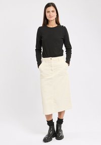 Haut noir à manches longues avec des boutons sur les épaules, associé à une jupe en velours côtelé beige jusqu'aux genoux. Bottines noires avec des chaussettes côtelées.