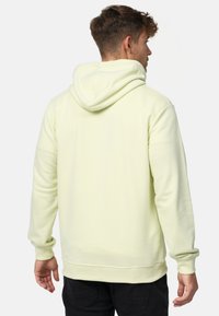 Lichtgeel hoodie met een zachte textuur, kangoeroe zak en verstelbare capuchon, voorzien van ribgebreide boorden en zoom. Zwarte broek zichtbaar.