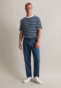 Chemise à rayures bleu marine et blanche à manches courtes, coupe décontractée, associée à un pantalon bleu marine à cordon de serrage et des baskets blanches. Tenue simple et décontractée.